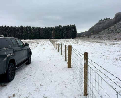 Stock fencing installed in snow beside forestry machinery near Tomatin
